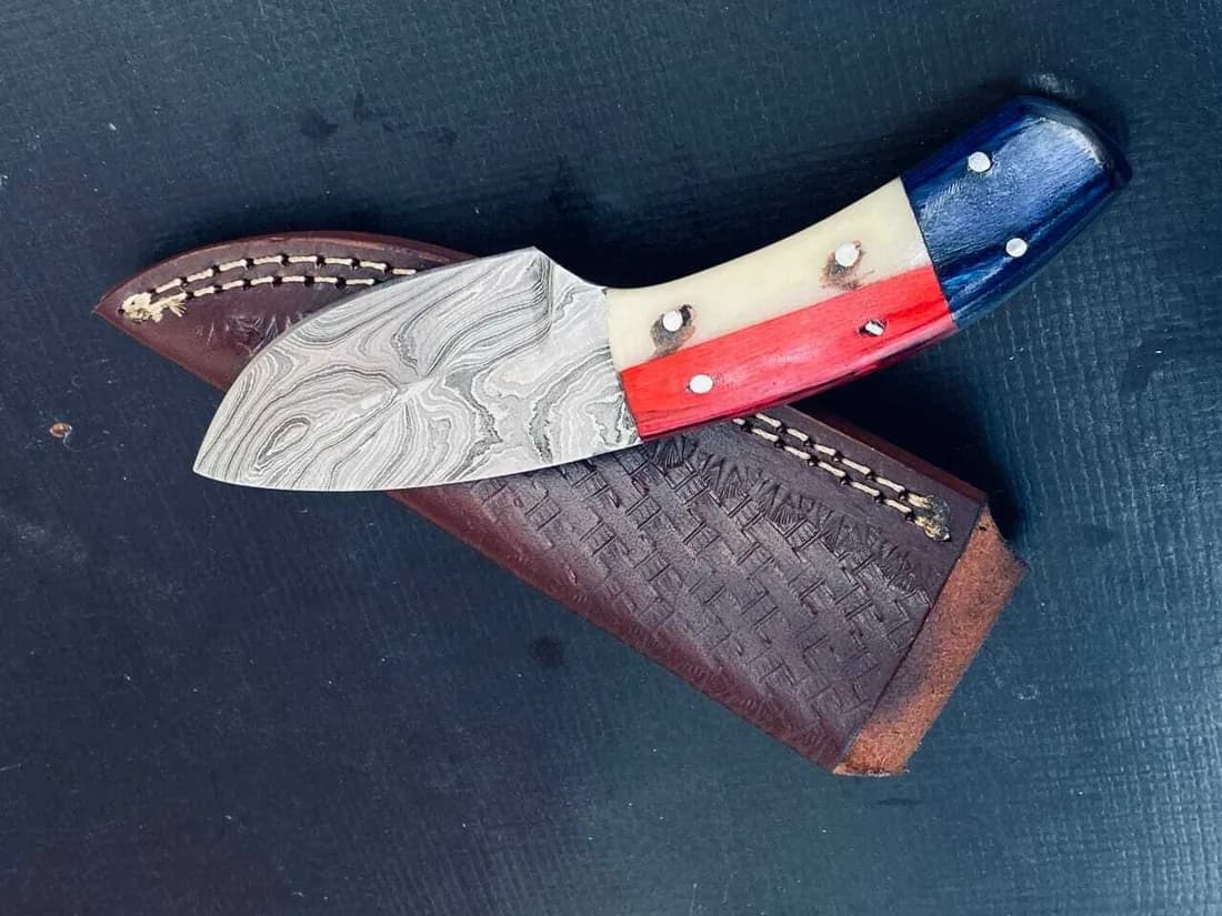 Custom Damascus knife with coloured handle beside a tooled basket-weave leather sheath
