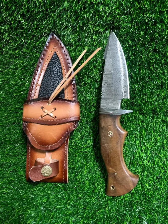 Damascus hunting knife beside a decorated leather knife sheath
